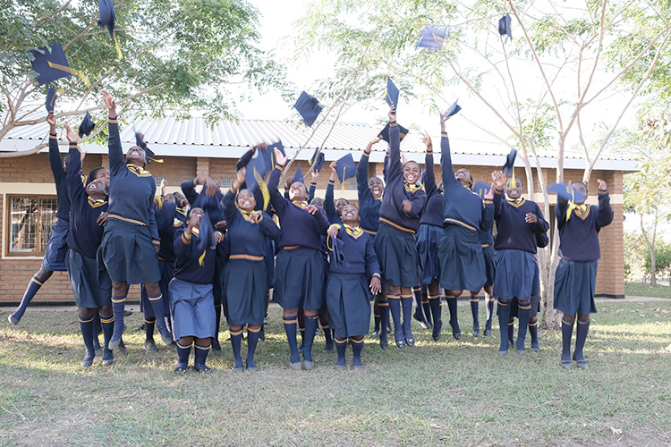 Kuwala form 4 girls in front of a classroom block jumping and throwing their graduation caps in the air. 