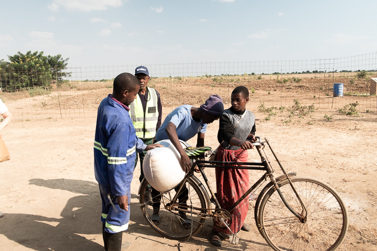 Local villagers gathered around a pedal bike with a sack of grain on the back of the bike ready to be milled.