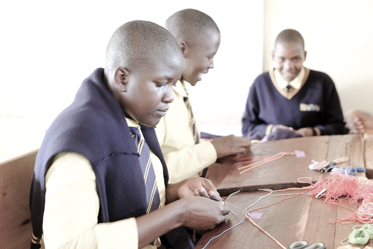 Kuwala students at a desk with a ball of yarn to make friendship bracelets.