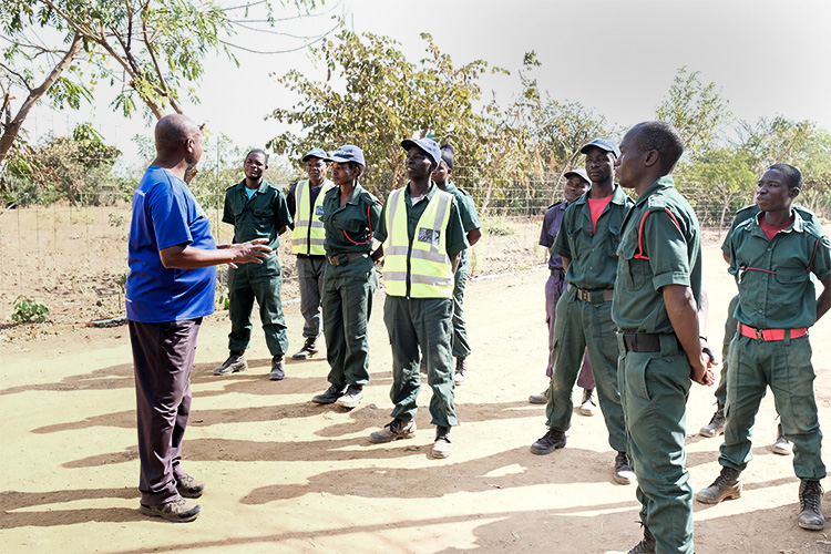 Kuwala security guards listening to security consultant outside next to the boarding fence. 